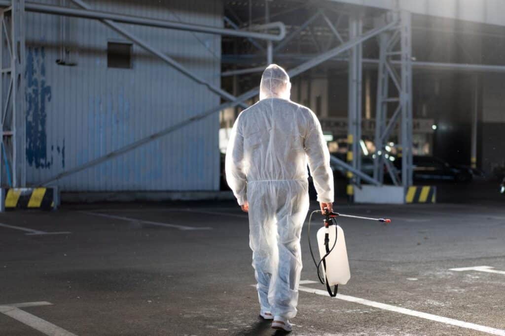Man dressed white protective overalls spraying surface